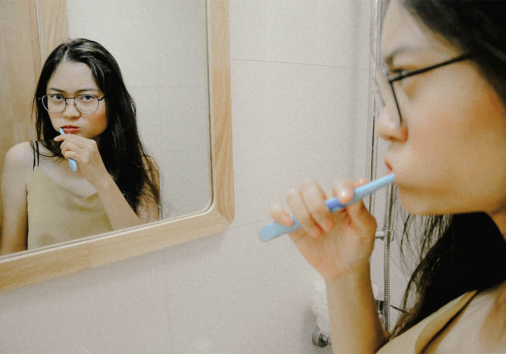 Tjej borstar tänderna i spegeln